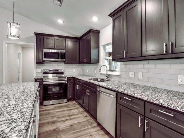 kitchen with stainless steel appliances, decorative light fixtures, light stone countertops, and a kitchen island