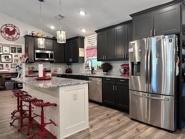 kitchen with tasteful backsplash, vaulted ceiling, a kitchen island, hanging light fixtures, and stainless steel appliances