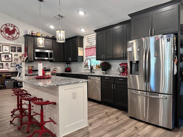 kitchen with a kitchen island, appliances with stainless steel finishes, sink, hanging light fixtures, and light stone countertops