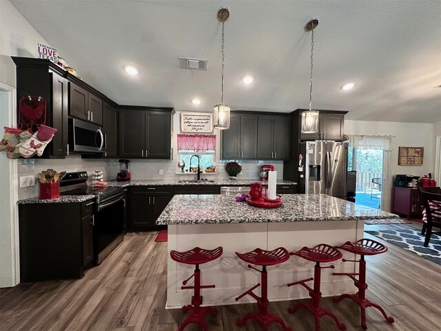 kitchen with sink, hanging light fixtures, a center island, stainless steel appliances, and light stone countertops