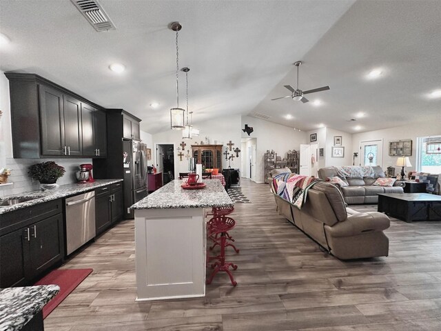 kitchen featuring a breakfast bar area, stainless steel appliances, hanging light fixtures, vaulted ceiling, and a center island