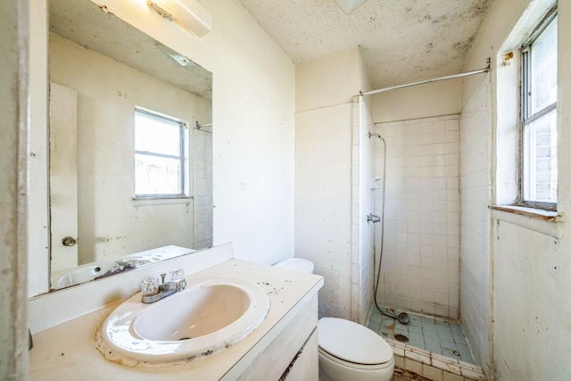 bathroom featuring toilet, tiled shower, vanity, and a textured ceiling