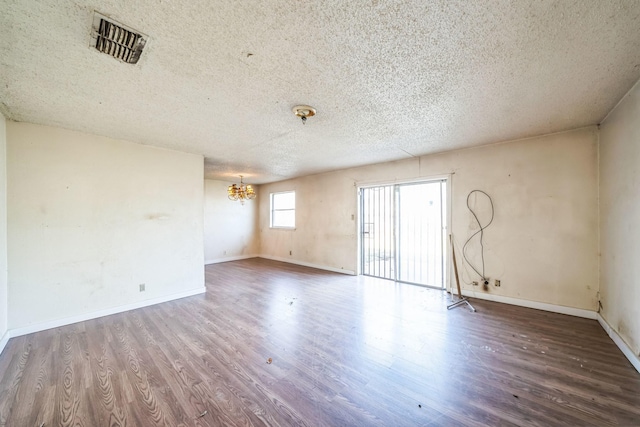 empty room featuring an inviting chandelier, a textured ceiling, and hardwood / wood-style floors