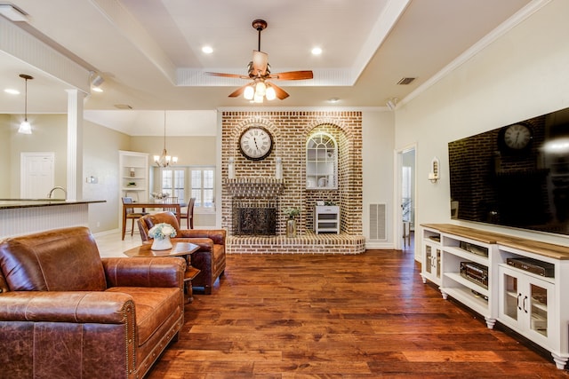 living area with ornamental molding, ceiling fan with notable chandelier, wood finished floors, a fireplace, and a raised ceiling