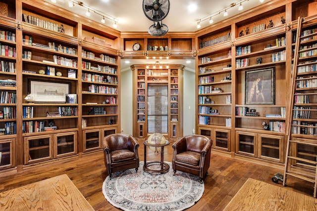sitting room with hardwood / wood-style flooring, rail lighting, built in features, and wall of books