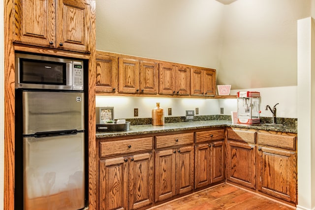 kitchen featuring a sink, stainless steel appliances, dark stone counters, light wood-style floors, and brown cabinetry