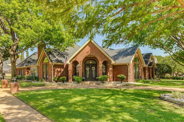 view of front of house featuring a front yard, french doors, brick siding, and roof with shingles