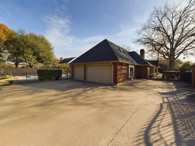 view of side of home featuring fence, driveway, an attached garage, a chimney, and brick siding