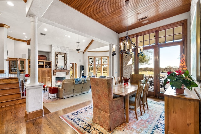 dining room featuring lofted ceiling, light hardwood / wood-style flooring, decorative columns, a fireplace, and ceiling fan with notable chandelier