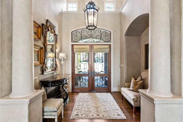 entrance foyer with a towering ceiling, dark hardwood / wood-style flooring, ornate columns, and french doors