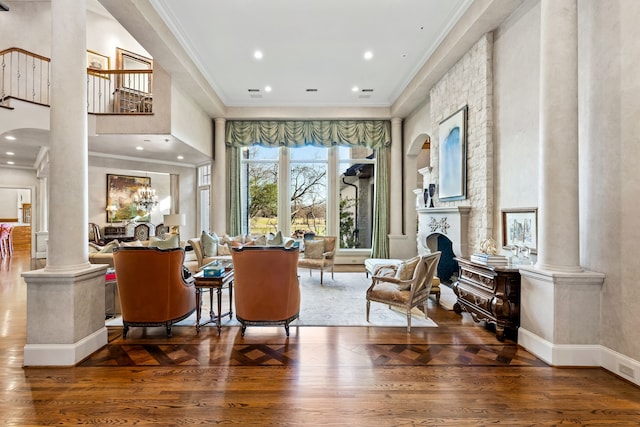 living area featuring decorative columns, crown molding, wood-type flooring, a notable chandelier, and a fireplace