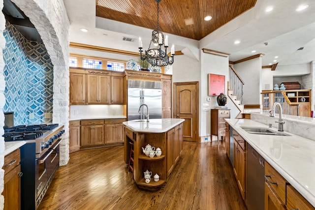 kitchen with high quality appliances, an island with sink, sink, dark hardwood / wood-style flooring, and hanging light fixtures