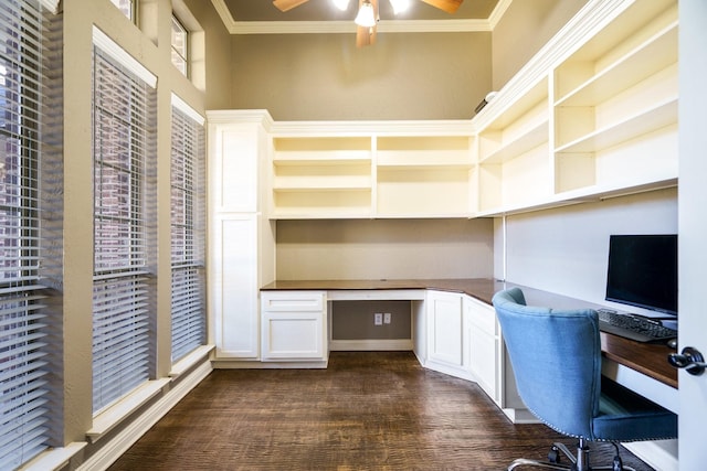 unfurnished office with ceiling fan, dark wood-type flooring, built in desk, and ornamental molding