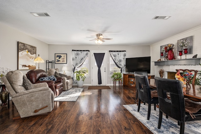 living room with ceiling fan, a fireplace, a textured ceiling, and dark wood-type flooring