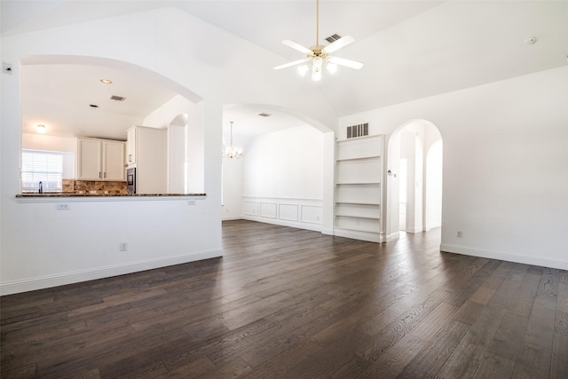 unfurnished living room featuring built in features, dark hardwood / wood-style flooring, ceiling fan with notable chandelier, and vaulted ceiling