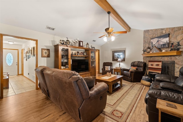 living room with light wood-type flooring, lofted ceiling with beams, a stone fireplace, and ceiling fan