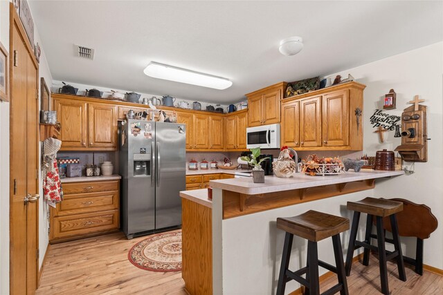 kitchen featuring a kitchen breakfast bar, kitchen peninsula, stainless steel fridge with ice dispenser, and light hardwood / wood-style floors