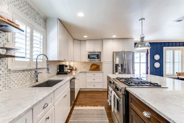 kitchen featuring appliances with stainless steel finishes, light stone counters, sink, white cabinetry, and hanging light fixtures