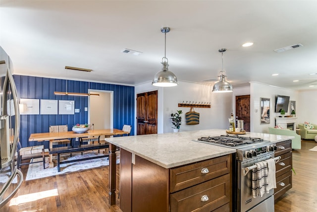 kitchen featuring a center island, stainless steel appliances, wood walls, decorative light fixtures, and light wood-type flooring