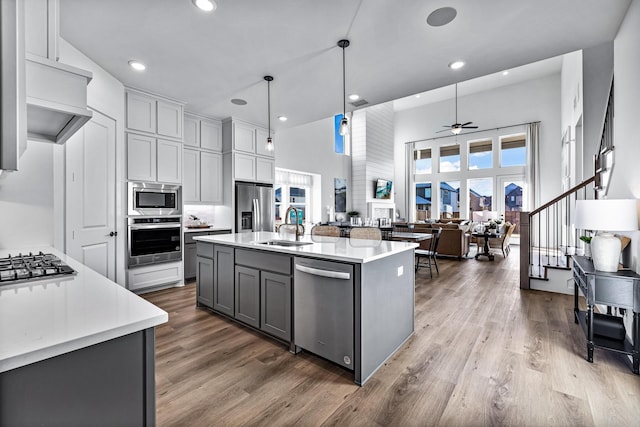 kitchen with appliances with stainless steel finishes, a towering ceiling, gray cabinetry, a kitchen island with sink, and hanging light fixtures