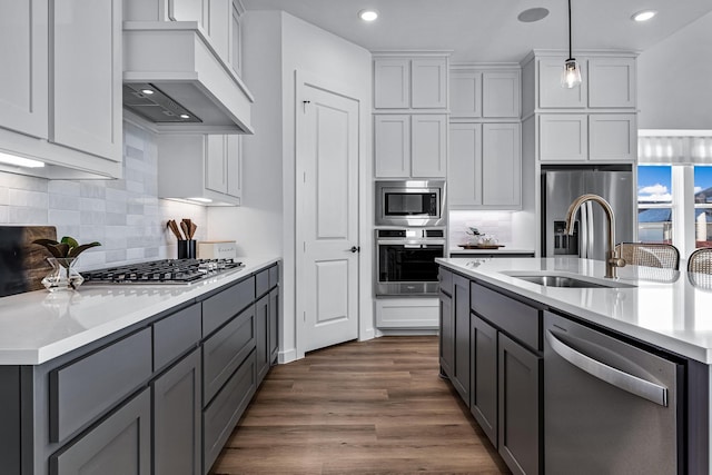 kitchen with dark wood-type flooring, sink, custom exhaust hood, hanging light fixtures, and appliances with stainless steel finishes