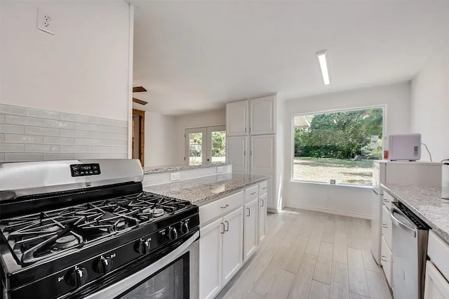 kitchen with light stone countertops, white cabinets, stainless steel appliances, and light hardwood / wood-style floors