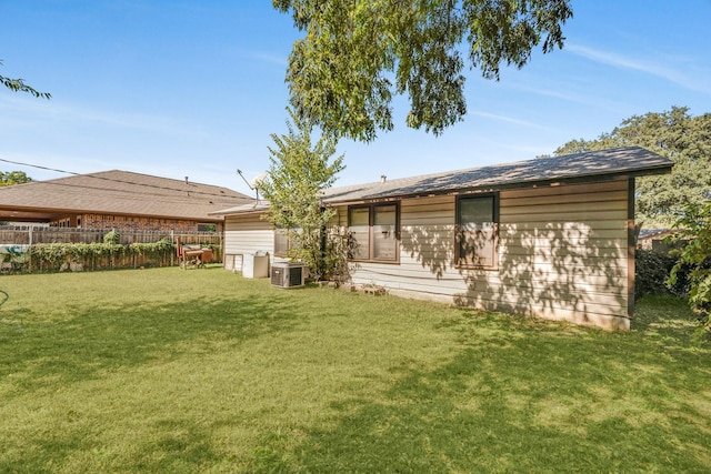 rear view of house with central air condition unit and a lawn