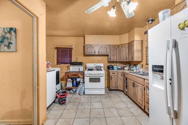 kitchen featuring sink, light tile patterned floors, white appliances, ceiling fan, and a textured ceiling