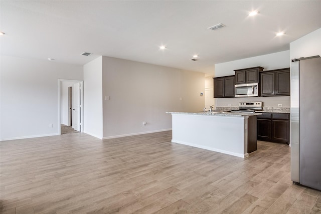 kitchen featuring dark brown cabinets, light hardwood / wood-style floors, stainless steel appliances, and an island with sink