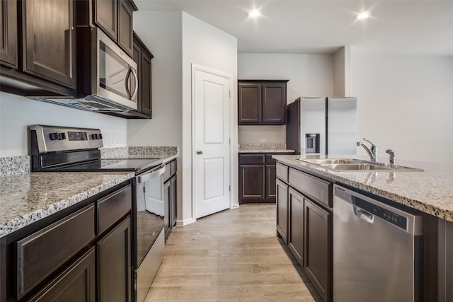 kitchen featuring sink, light stone countertops, appliances with stainless steel finishes, dark brown cabinets, and light hardwood / wood-style floors