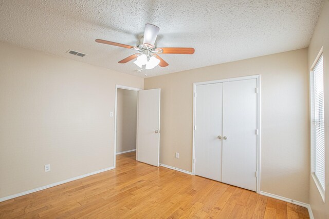 unfurnished bedroom featuring a textured ceiling, a closet, light hardwood / wood-style floors, and ceiling fan