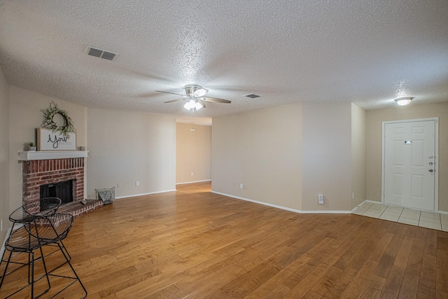 unfurnished living room with ceiling fan, light wood-type flooring, a textured ceiling, and a brick fireplace