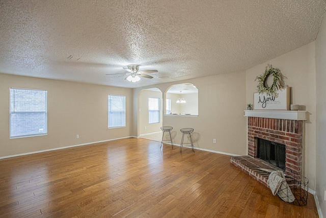 unfurnished living room with hardwood / wood-style flooring, ceiling fan, a textured ceiling, and a brick fireplace