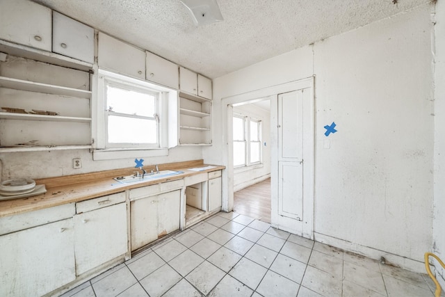 kitchen with white cabinetry, sink, light tile patterned flooring, and a textured ceiling