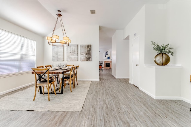 dining area featuring a notable chandelier, wood-type flooring, a fireplace, and vaulted ceiling