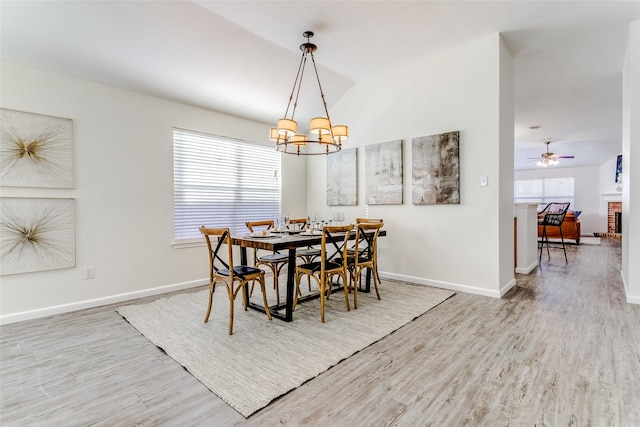 dining room featuring a brick fireplace, ceiling fan with notable chandelier, and light hardwood / wood-style flooring