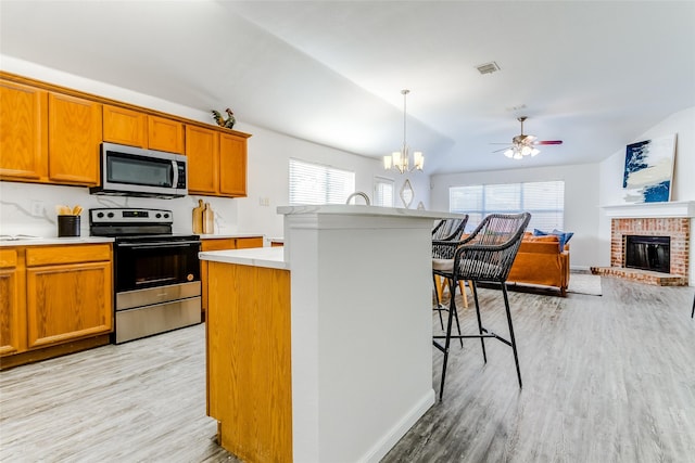 kitchen with a kitchen bar, light wood-type flooring, stainless steel appliances, a fireplace, and a center island