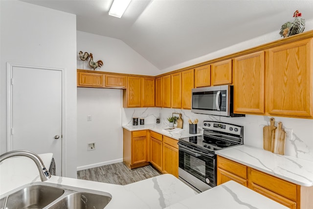 kitchen with light stone counters, sink, stainless steel appliances, and vaulted ceiling