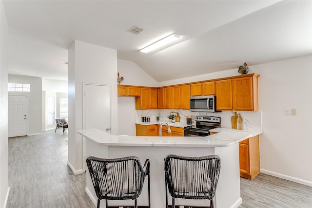 kitchen with stainless steel appliances, light hardwood / wood-style flooring, kitchen peninsula, lofted ceiling, and a breakfast bar area