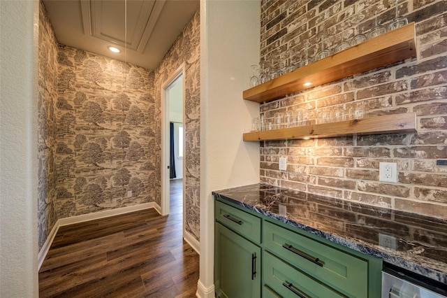 bar featuring dark wood-type flooring, dark stone counters, brick wall, and green cabinets