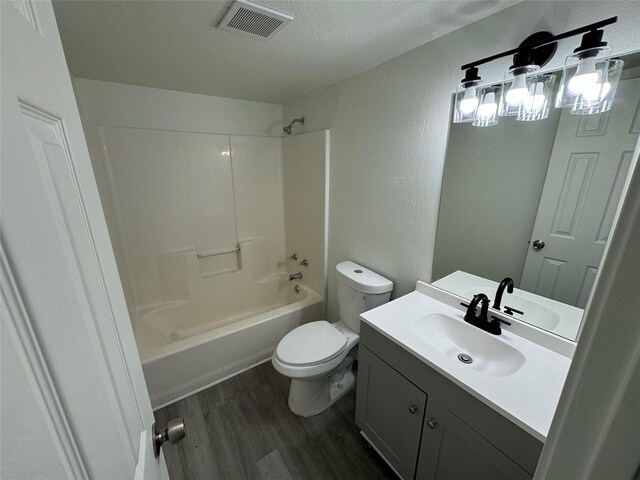 full bathroom with hardwood / wood-style floors, washtub / shower combination, vanity, toilet, and a textured ceiling