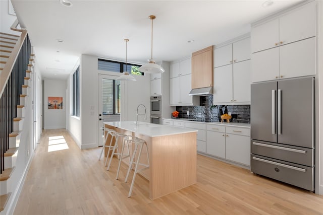 kitchen featuring decorative light fixtures, white cabinetry, a kitchen breakfast bar, stainless steel appliances, and a center island with sink