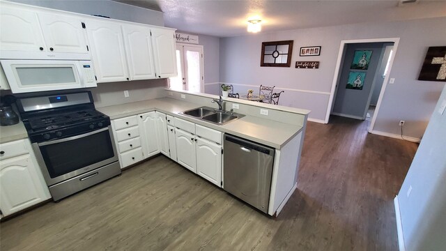 kitchen with white cabinets, sink, dark hardwood / wood-style floors, appliances with stainless steel finishes, and kitchen peninsula