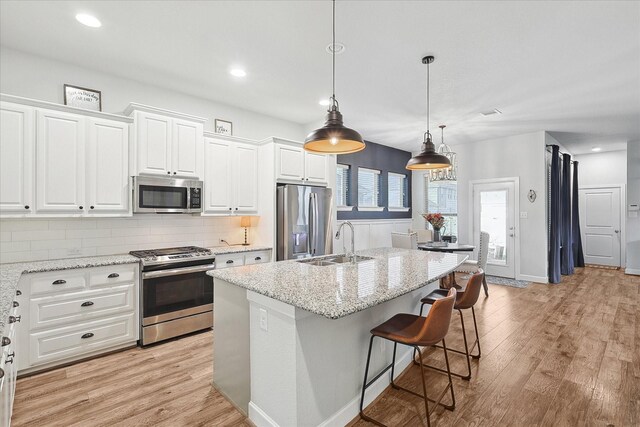 kitchen with light stone countertops, appliances with stainless steel finishes, pendant lighting, a center island with sink, and white cabinets