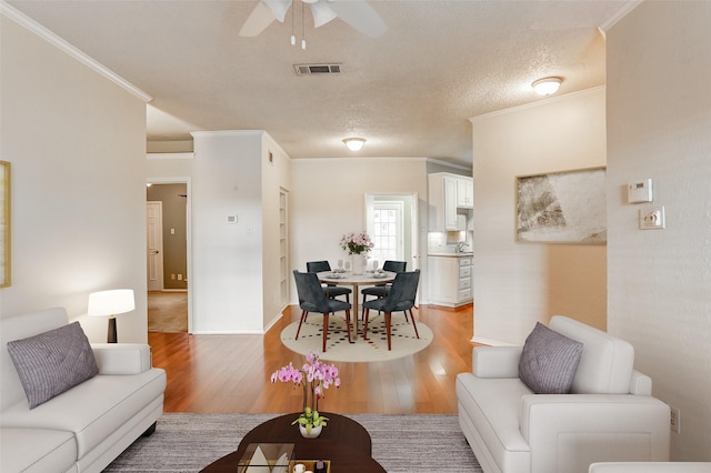 living room featuring a textured ceiling, hardwood / wood-style flooring, ceiling fan, and ornamental molding