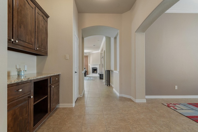 bar featuring light stone counters, dark brown cabinetry, crown molding, and light tile patterned floors