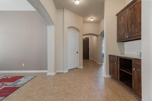 kitchen with dark brown cabinets, light stone counters, crown molding, and light tile patterned flooring