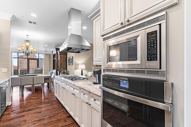 kitchen featuring an inviting chandelier, wall chimney exhaust hood, dark hardwood / wood-style floors, light stone countertops, and appliances with stainless steel finishes