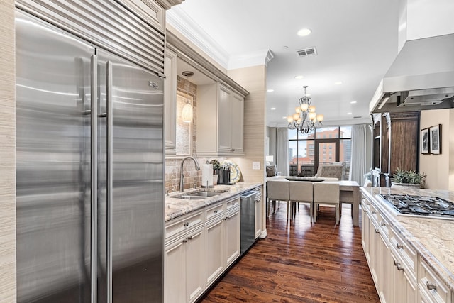 kitchen featuring island exhaust hood, light stone countertops, stainless steel appliances, sink, and a notable chandelier