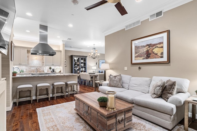 living room with dark wood-type flooring, ceiling fan with notable chandelier, and ornamental molding